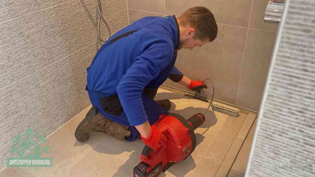 Een monteur ontstopt een langwerpige douchegoot met een elektrische veer, een doucheputje verstopt door haren en zeep in Voorburg