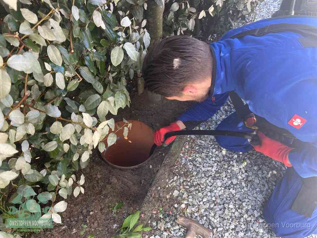 Een monteur voert een slang in een geopende rioolput in de tuin om het hoofdriool te ontstoppen in Voorburg