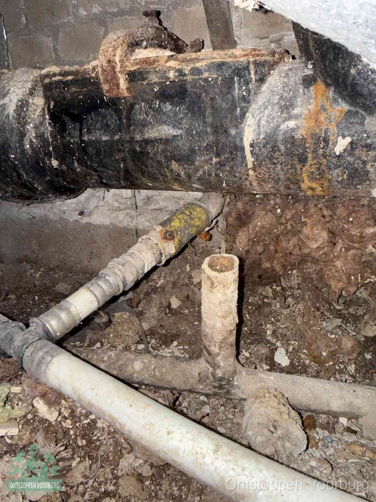 Een oude hoofdrioolbuis met roest- en kalkaanslag in een kruipruimte, oorzaak van terugkerende structurele rioolproblemen in Voorburg